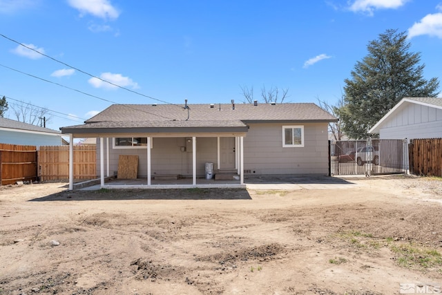 rear view of property featuring a gate, a shingled roof, fence, and a patio