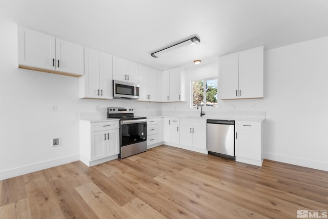 kitchen featuring white cabinetry, light countertops, light wood-type flooring, baseboards, and appliances with stainless steel finishes
