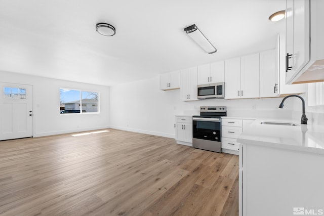 kitchen featuring white cabinetry, light countertops, a sink, light wood-style floors, and appliances with stainless steel finishes