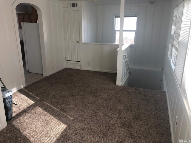carpeted empty room featuring arched walkways, visible vents, and tile patterned flooring