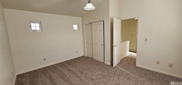 unfurnished bedroom featuring baseboards, dark carpet, vaulted ceiling, and a closet