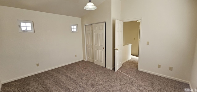 unfurnished bedroom featuring baseboards, multiple windows, vaulted ceiling, and dark carpet
