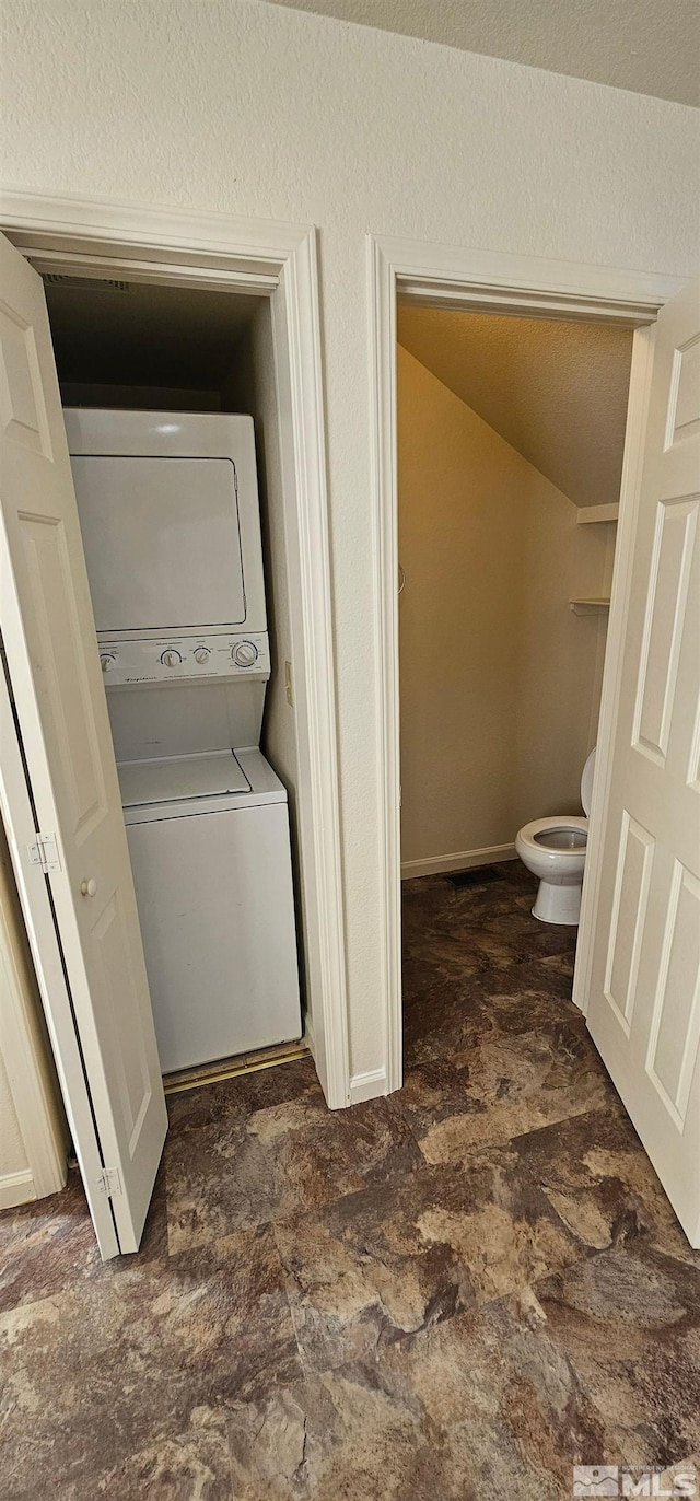 laundry room featuring baseboards, stacked washing maching and dryer, laundry area, and a textured ceiling