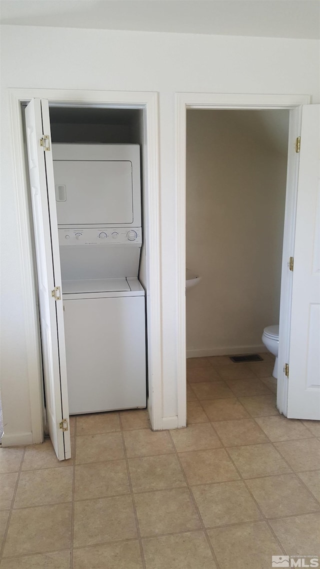 clothes washing area featuring light tile patterned flooring, visible vents, baseboards, stacked washer / drying machine, and laundry area