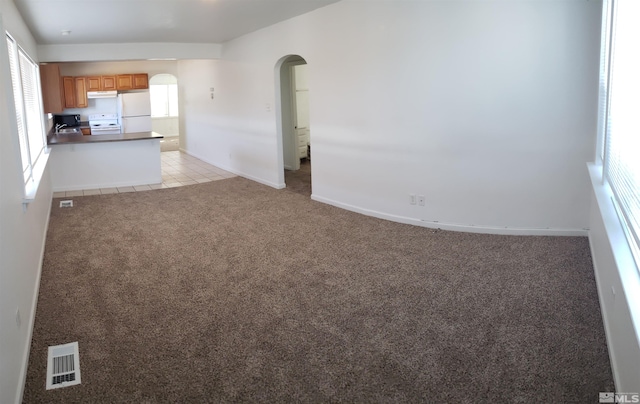 unfurnished living room with visible vents, baseboards, arched walkways, light tile patterned floors, and light colored carpet
