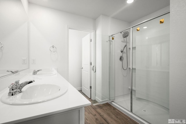bathroom with double vanity, a sink, a stall shower, and wood finished floors