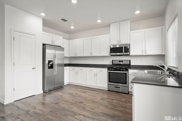 kitchen with visible vents, stainless steel appliances, dark countertops, dark wood finished floors, and a sink