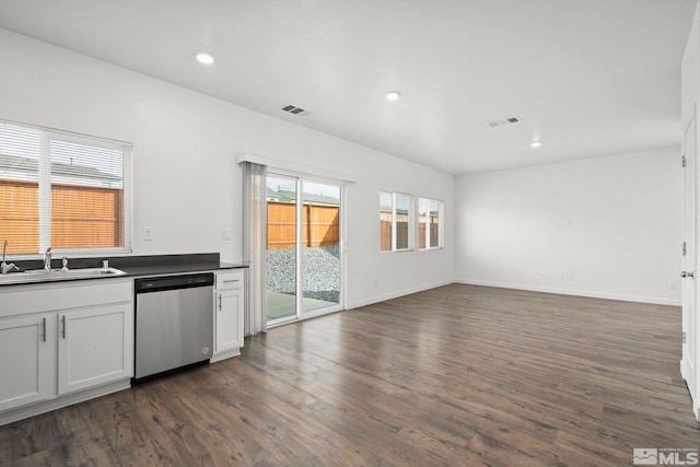 kitchen featuring dark wood-type flooring, stainless steel dishwasher, a sink, dark countertops, and visible vents