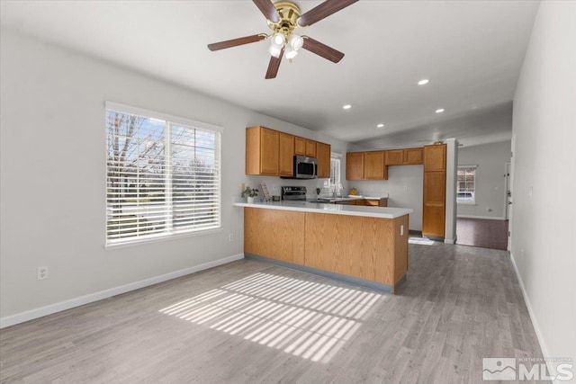 kitchen with light countertops, light wood-style floors, a peninsula, appliances with stainless steel finishes, and brown cabinetry