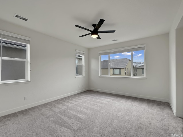 carpeted empty room with baseboards, visible vents, and a ceiling fan