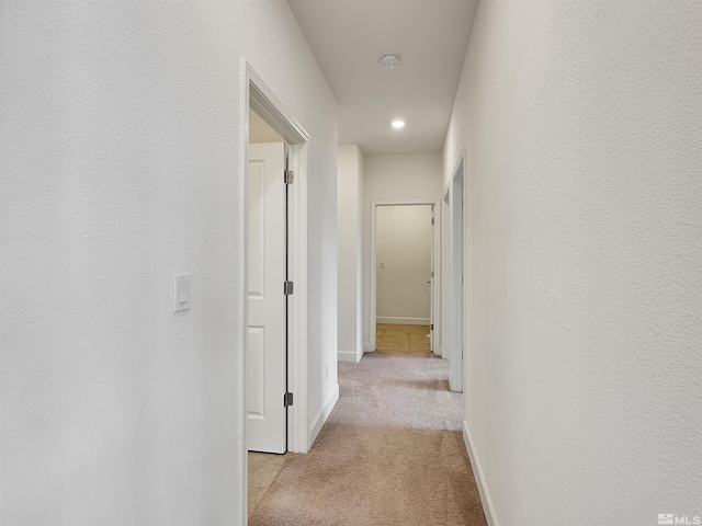 hallway featuring light colored carpet and baseboards