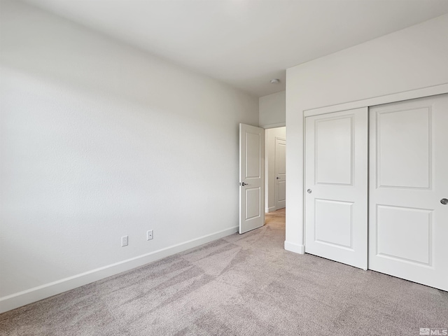 unfurnished bedroom with baseboards, a closet, and light colored carpet