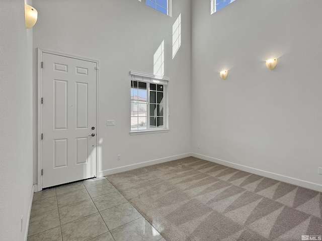 tiled entryway featuring carpet flooring, baseboards, and a high ceiling