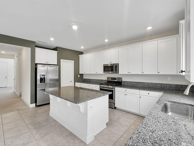 kitchen featuring dark stone counters, a kitchen island, a sink, white cabinets, and appliances with stainless steel finishes