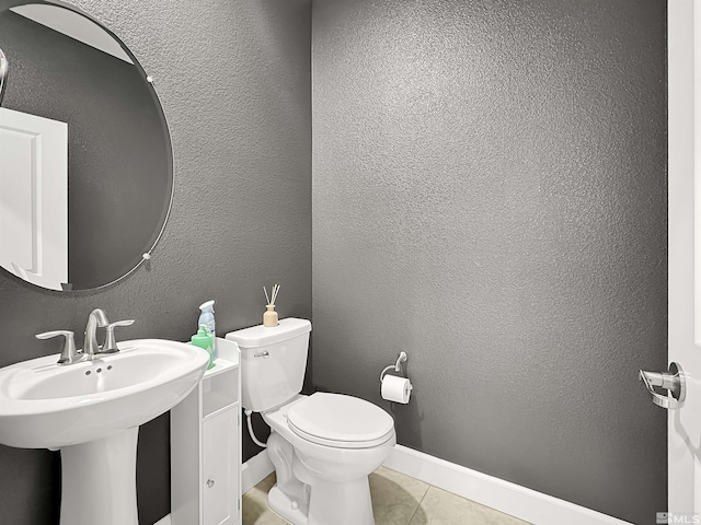 bathroom with tile patterned floors, toilet, a sink, baseboards, and a textured wall