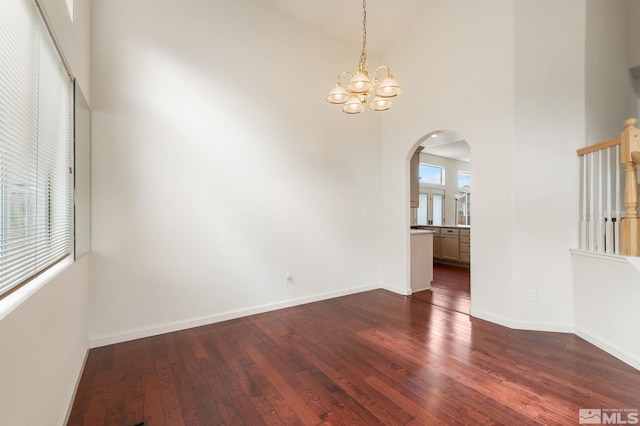 unfurnished room with a towering ceiling, arched walkways, dark wood-type flooring, and a chandelier
