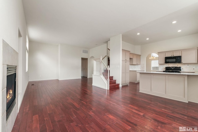 unfurnished living room featuring stairway, recessed lighting, dark wood-style flooring, visible vents, and a warm lit fireplace