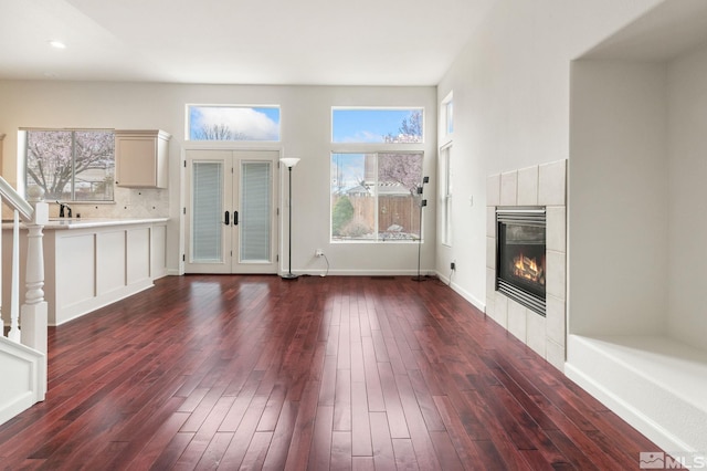 unfurnished living room featuring baseboards, dark wood-style floors, a tile fireplace, and french doors