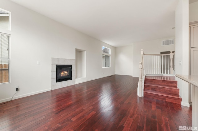 unfurnished living room with stairs, visible vents, a tile fireplace, and wood-type flooring