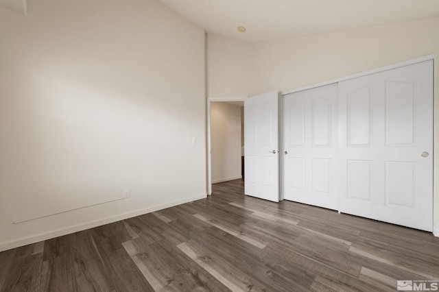 unfurnished bedroom featuring high vaulted ceiling, baseboards, a closet, and wood finished floors