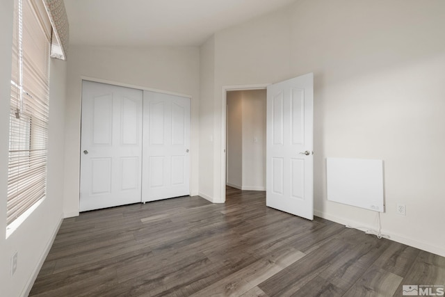unfurnished bedroom featuring a closet, lofted ceiling, dark wood-style floors, and baseboards