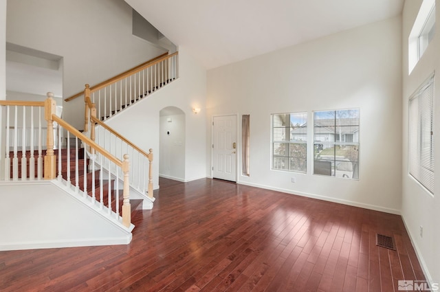 foyer entrance featuring stairs, wood finished floors, baseboards, visible vents, and a towering ceiling
