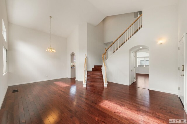 unfurnished living room featuring stairs, arched walkways, a towering ceiling, and wood-type flooring