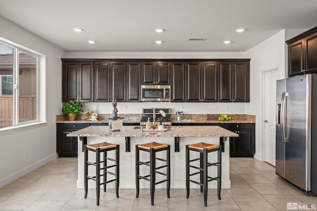 kitchen featuring light stone countertops, a kitchen bar, stainless steel appliances, a center island with sink, and a sink