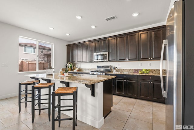 kitchen with stainless steel appliances, light stone countertops, a sink, visible vents, and a kitchen island with sink
