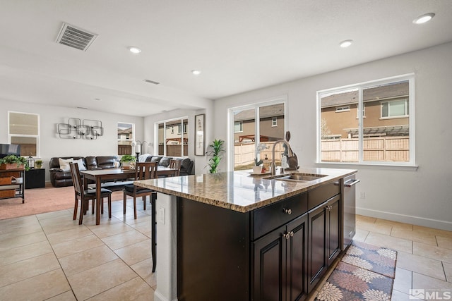 kitchen with a sink, light stone countertops, open floor plan, a kitchen island with sink, and visible vents