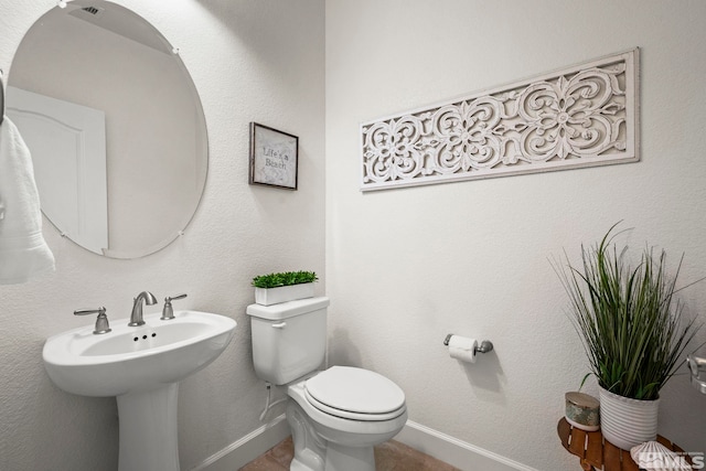 half bathroom with toilet, a sink, and baseboards