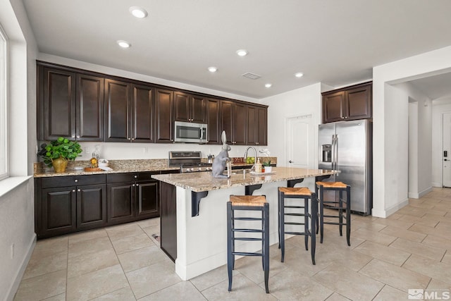 kitchen with visible vents, a breakfast bar, light stone countertops, a kitchen island with sink, and appliances with stainless steel finishes