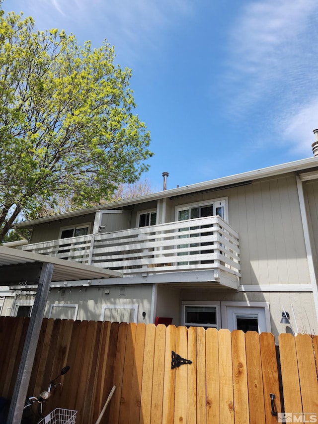 rear view of house with a gate, a balcony, and fence