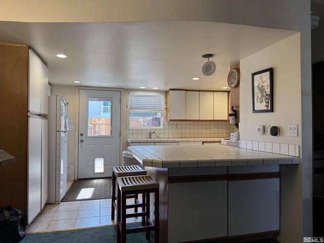 kitchen with backsplash, a breakfast bar, light tile patterned floors, freestanding refrigerator, and a peninsula