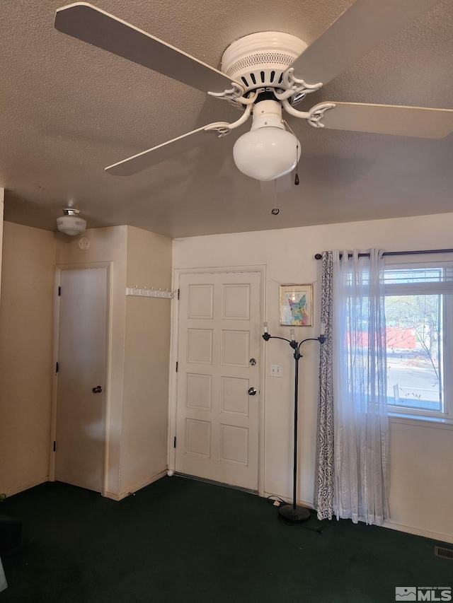 entryway with dark carpet, a ceiling fan, and a textured ceiling
