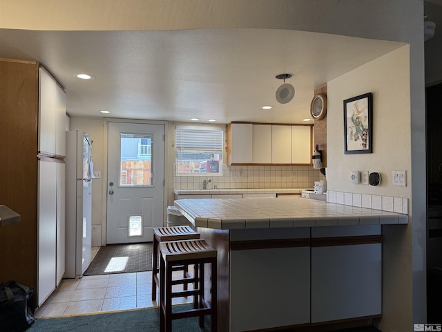 kitchen with backsplash, a breakfast bar, light tile patterned floors, freestanding refrigerator, and a peninsula