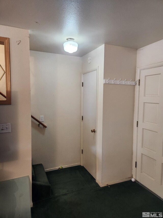 hall featuring dark colored carpet, baseboards, and a textured ceiling