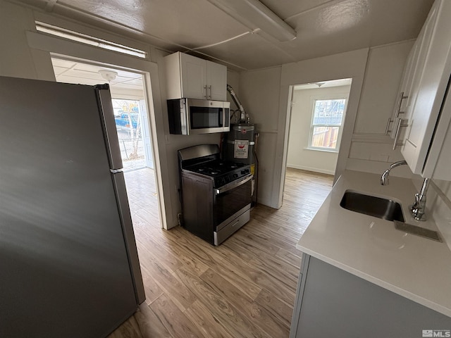 kitchen with a sink, light countertops, white cabinetry, stainless steel appliances, and light wood-style flooring