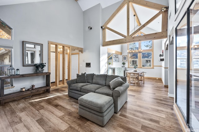 living room with high vaulted ceiling, baseboards, an inviting chandelier, and wood finished floors