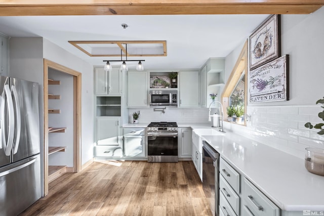 kitchen with open shelves, a sink, light countertops, wood finished floors, and stainless steel appliances