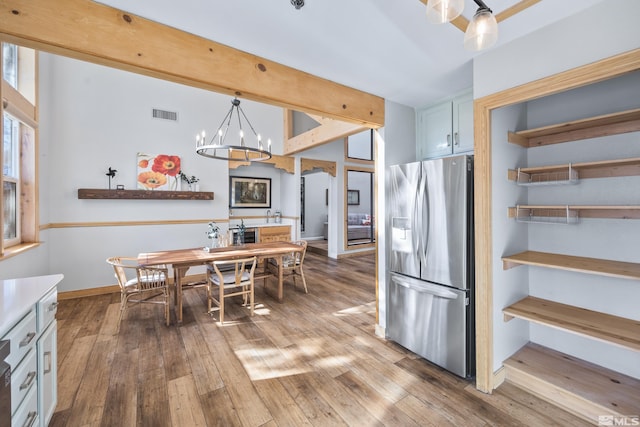 dining space with visible vents, wood-type flooring, a chandelier, and beamed ceiling
