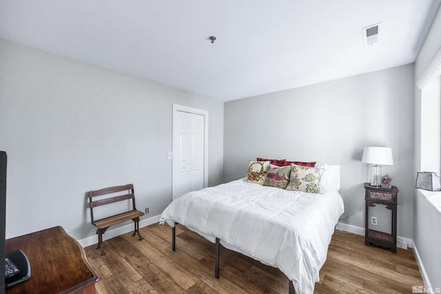 bedroom with visible vents, baseboards, a closet, and wood finished floors