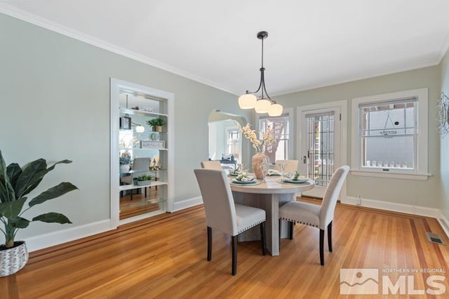 dining space with light wood-style flooring, arched walkways, ornamental molding, visible vents, and baseboards