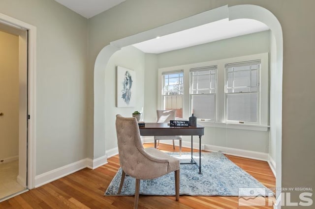 office space with arched walkways, wood finished floors, and baseboards