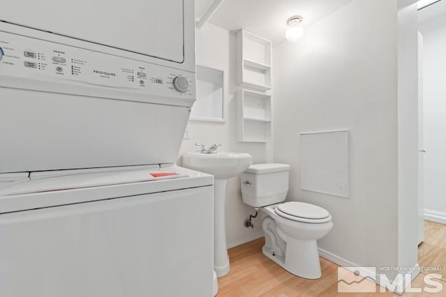 bathroom with stacked washer and dryer, toilet, wood finished floors, and baseboards