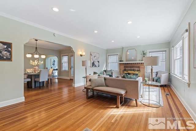 living area featuring crown molding, arched walkways, a brick fireplace, light wood finished floors, and baseboards