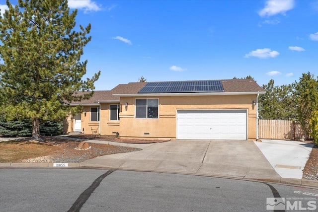ranch-style house featuring roof mounted solar panels, a garage, fence, concrete driveway, and stucco siding