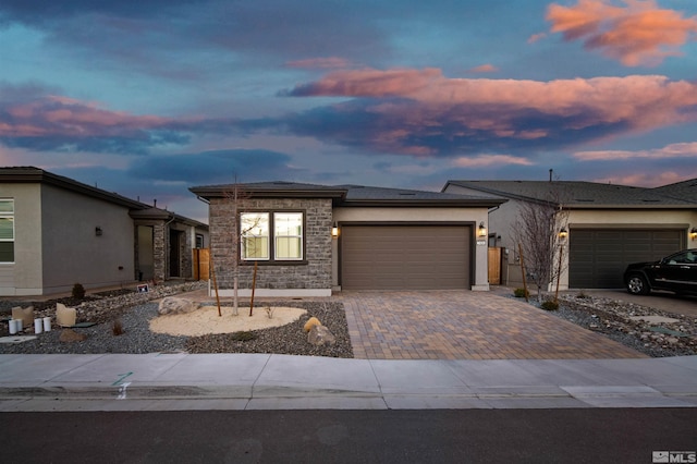 view of front of home with stucco siding, stone siding, decorative driveway, an attached garage, and solar panels