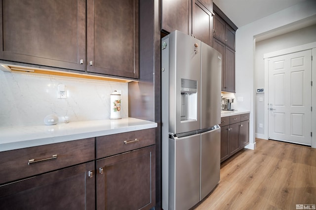 kitchen featuring light wood-style floors, dark brown cabinetry, tasteful backsplash, light stone counters, and stainless steel fridge