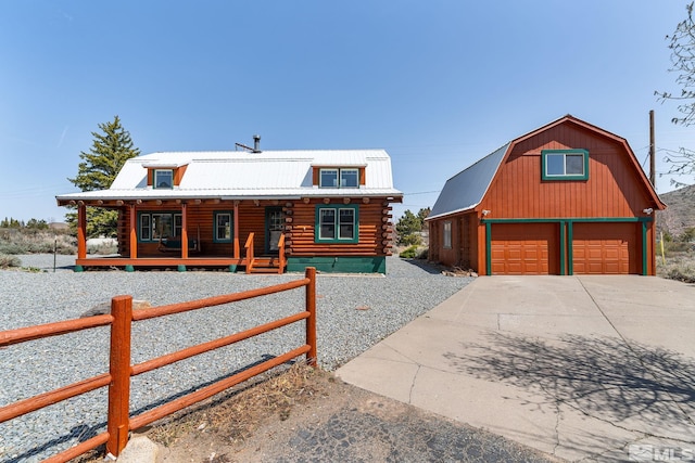log-style house with a detached garage, a fenced front yard, log exterior, an outbuilding, and covered porch